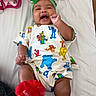 baby, infant, smiling, laughing, green_headband, red_sock, sesame_street_clothing, bed, blanket, pink_blanket, happy, child, person, cute, indoor, lying_down, playful, colorful_clothing, head_accessory, footwear