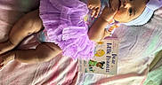 Daelani joined the competition — help win amazing prizes! baby, tutu, headband, book, blanket, pastel_colors, infant, smiling, cute, child, laying_down, purple, dress, soft_texture, indoors, chubby_legs, happy, portrait, person, reading