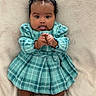 Daelani is registered to the contest to win money with this photo: baby, child, infant, plaid_dress, teal, tongue_out, cute, soft_blanket, lying_down, hands, clenched_hands, curly_hair, hair_bow, playful, adorable, skin, face, portrait, indoors, expression