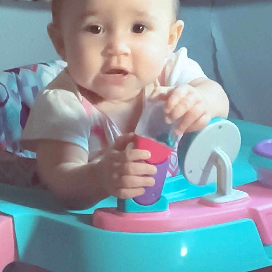 Nevaeh is registered to the contest to win money with this photo: baby, child, infant, sitting, activity_center, toy, playtime, portrait, face, eyes, curious, indoor, home, colorful, pink, blue, leopard_print, clothing, smiling, text_overlay