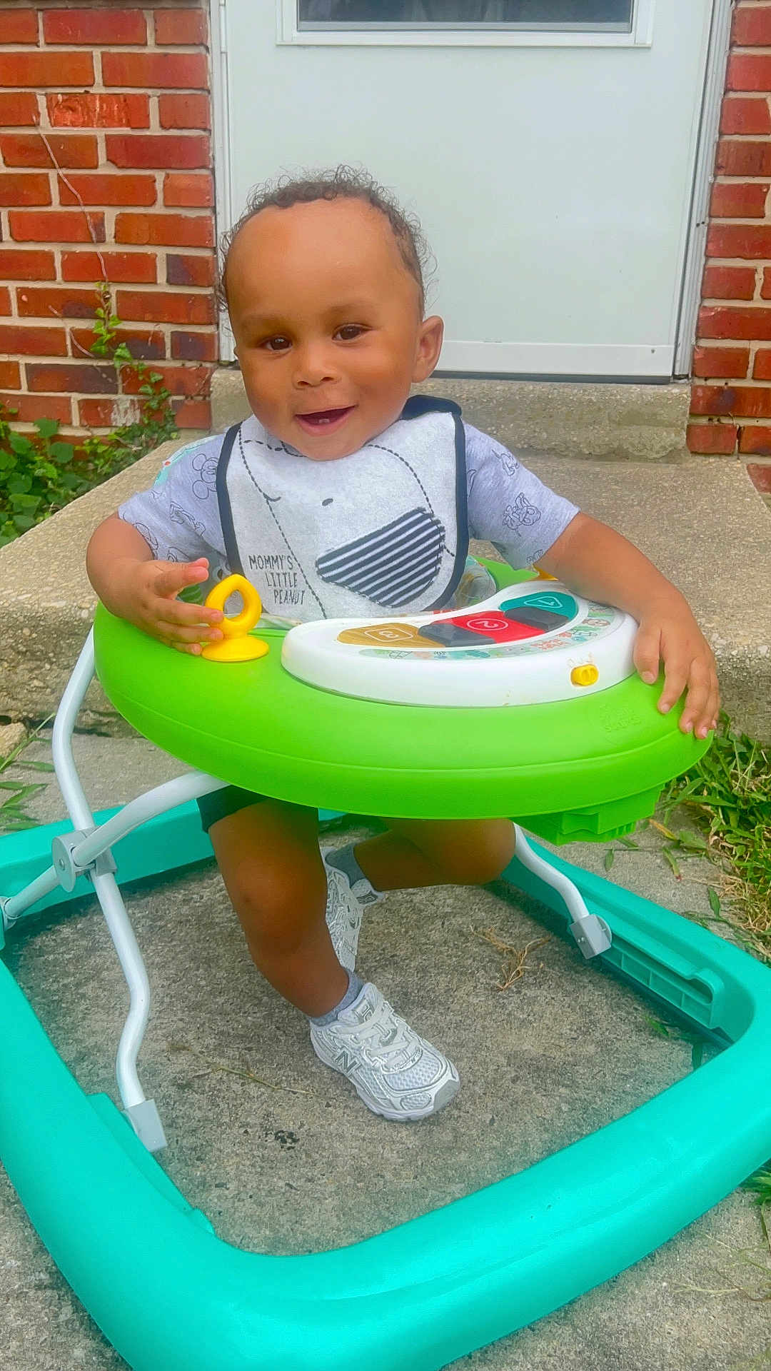 Amar is registered to the contest to win money with this photo: toddler, child, walker, toy, smiling, outdoor, concrete, brick_wall, door, shoes, sneakers, grass, play, baby, person, clothing, happy, cute, young, front_porch