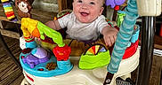 Hannah joined the competition — help win amazing prizes! baby, smiling, activity_jumper, toy, colorful, happy, infant, wooden_floor, bench, indoor, child, playtime, face, person, seat, floor_mat, decor, purple_toy, red_toy, green_toy