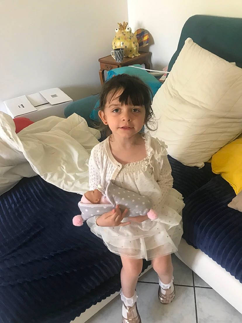Heilly participe au concours pour gagner de l'argent avec cette photo : baby_toddler_clothing, comfort, couch, dress, face, flooring, fun, hair, happy, human_leg, lamp, leg, linens, living_room, person, pillow, room, textile, thigh, toddler