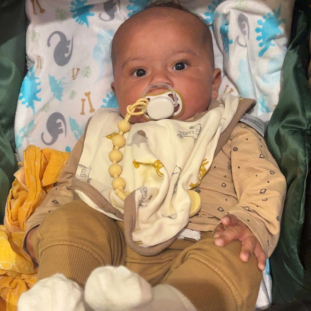 Lenny a rejoint le concours — aidez-le/la à gagner de superbes lots ! baby, blanket, child, clothing, cozy, curious, cute, dinosaur_pattern, eyes, face, head, indoors, infant, pacifier, person, seated, small_hand, socks, stroller, warm_colors