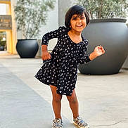 Ziona Yennam is registered to the contest to win money with this photo: background_blur, black_dress, casual_clothing, child, concrete, daylight, girl, happy, hearts_pattern, modern_building, outdoor, person, playful_pose, portrait, potted_plants, short_hair, silver_shoes, smiling, standing, urban