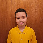 David joined the competition — help win amazing prizes! child, boy, smile, yellow_shirt, polo_shirt, short_hair, indoors, wooden_background, portrait, casual_clothing, standing, person, face, young, happy, front_view, brown_hair, buttoned_shirt, single_person, light_skin
