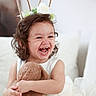 child, toddler, laughing, curly_hair, bunny_ears, headband, teddy_bear, white_dress, couch, cushion, smile, happy, indoor, plush_toy, portrait, cute, soft_fabric, sitting, decor, person