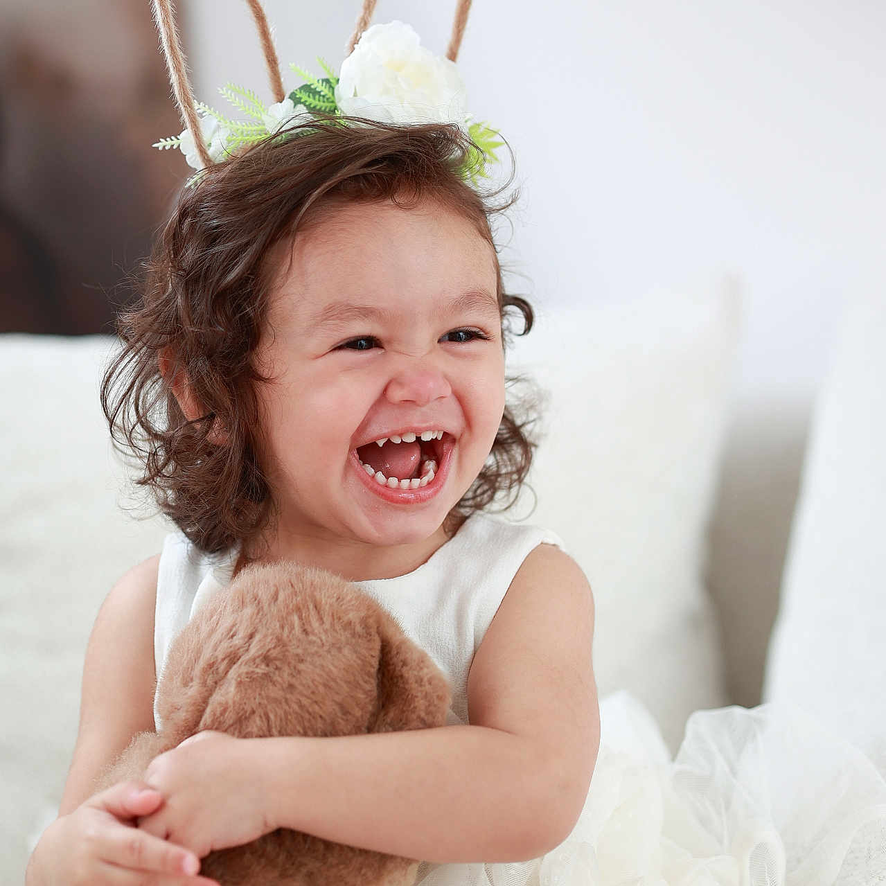 Leria participe au concours pour gagner de l'argent avec cette photo : child, toddler, laughing, curly_hair, bunny_ears, headband, teddy_bear, white_dress, couch, cushion, smile, happy, indoor, plush_toy, portrait, cute, soft_fabric, sitting, decor, person