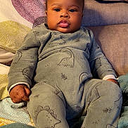 Joshua a rejoint le concours — aidez-le/la à gagner de superbes lots ! baby, infant, child, onesie, dinosaur_pattern, couch, blanket, pillow, indoors, cute, chubby_cheeks, relaxed, cozy, soft_fabric, portrait, young_child, seated, home, sleepwear, comfortable