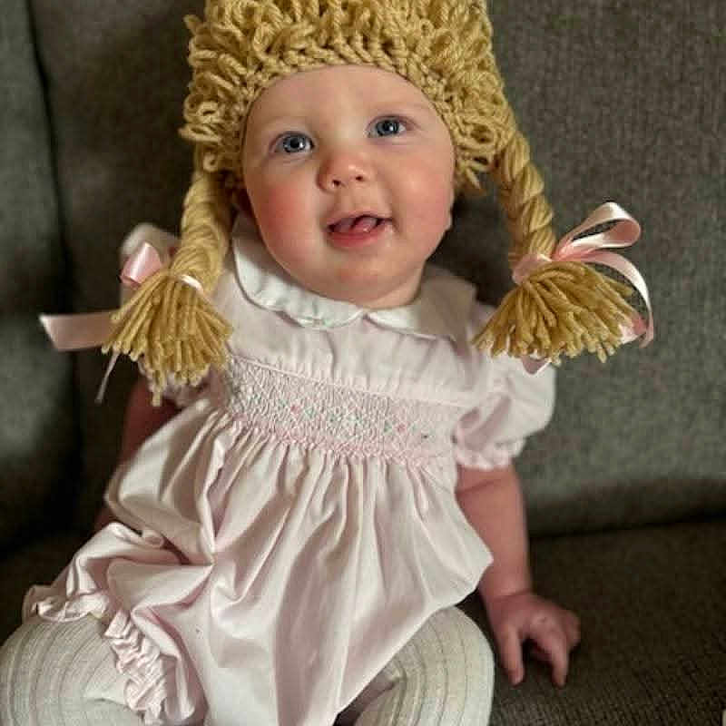 Jouney joined the competition — help win amazing prizes! baby, blue_eyes, child, couch, cozy, cute, face, happy, indoor, infant, pigtails, pink_dress, pink_ribbons, playful, portrait, sitting, smiling, soft_lighting, white_tights, yarn_wig