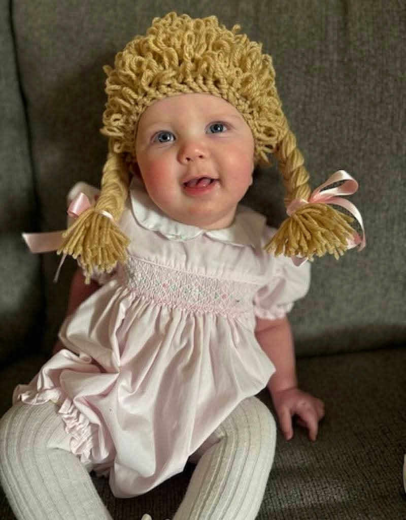 Jouney joined the competition — help win amazing prizes! baby, blue_eyes, child, couch, cozy, cute, face, happy, indoor, infant, pigtails, pink_dress, pink_ribbons, playful, portrait, sitting, smiling, soft_lighting, white_tights, yarn_wig