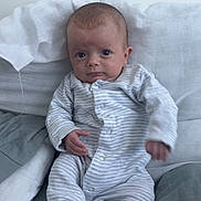 Mateo joined the competition — help win amazing prizes! baby, infant, onesie, striped_clothing, pillow, blanket, sitting, indoors, face, expression, hand, footed_pajamas, soft_fabric, cute, child, person, young, casual, relaxed, comfort