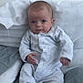 baby, infant, onesie, striped_clothing, pillow, blanket, sitting, indoors, face, expression, hand, footed_pajamas, soft_fabric, cute, child, person, young, casual, relaxed, comfort