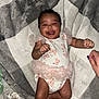baby, smiling, infant, onesie, butterflies, blanket, happy, lying_down, cute, child, frills, hand, skin, fabric, cozy, expression, playful, person, newborn, sleepwear