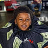 child, boy, haircut, barber_cape, dollar_bills, smiling, portrait, barbershop, person, face, hair, clothing, happy, indoor, sitting, black_hair, young, casual, people, background