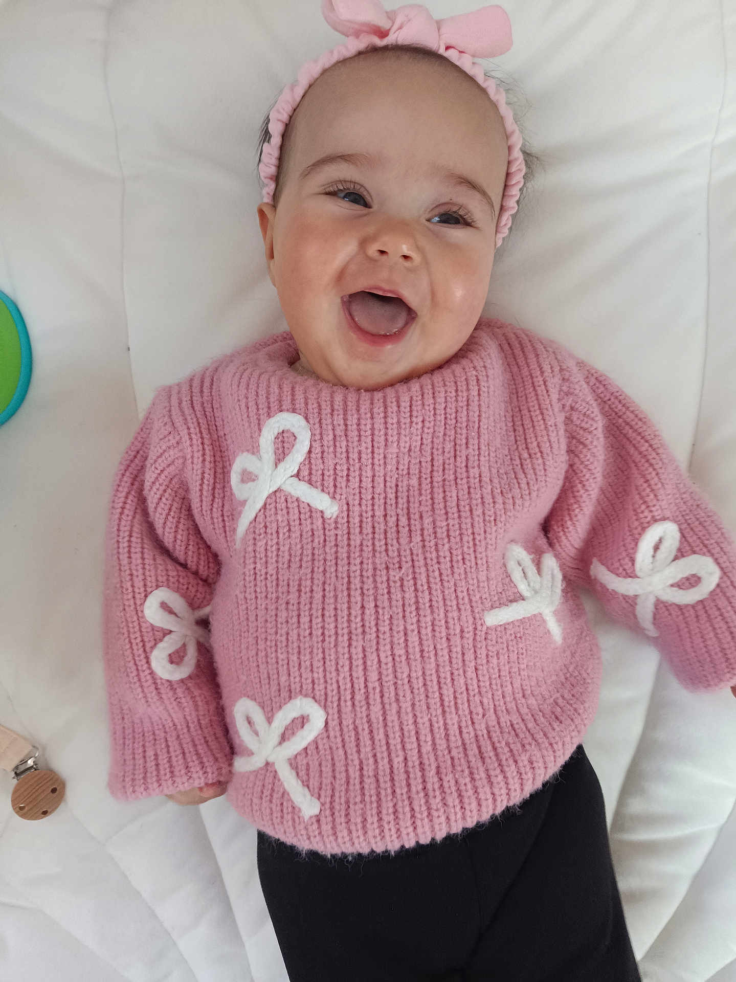Joye a rejoint le concours — aidez-le/la à gagner de superbes lots ! baby, smiling, pink_sweater, headband, white_bows, lying_down, happy, infant, cute, child, indoor, soft_surface, black_pants, closeup, portrait, person, toddler, young_child, apparel, playful