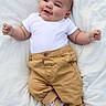 adorable, baby, baby_face, blanket, casual, child, clothing, cute, happy, infant, infant_fashion, lying_down, newborn, portrait, shoes, small_hands, smiling, soft_texture, tan_pants, white_onesie