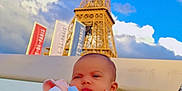 Ella a rejoint le concours — aidez-le/la à gagner de superbes lots ! arm, baby, bib, blanket, bracelet, child, cloud, daylight, eiffel_tower, expression, hand, holding, landmark, outdoor, person, portrait, sky, tourist, travel, watch