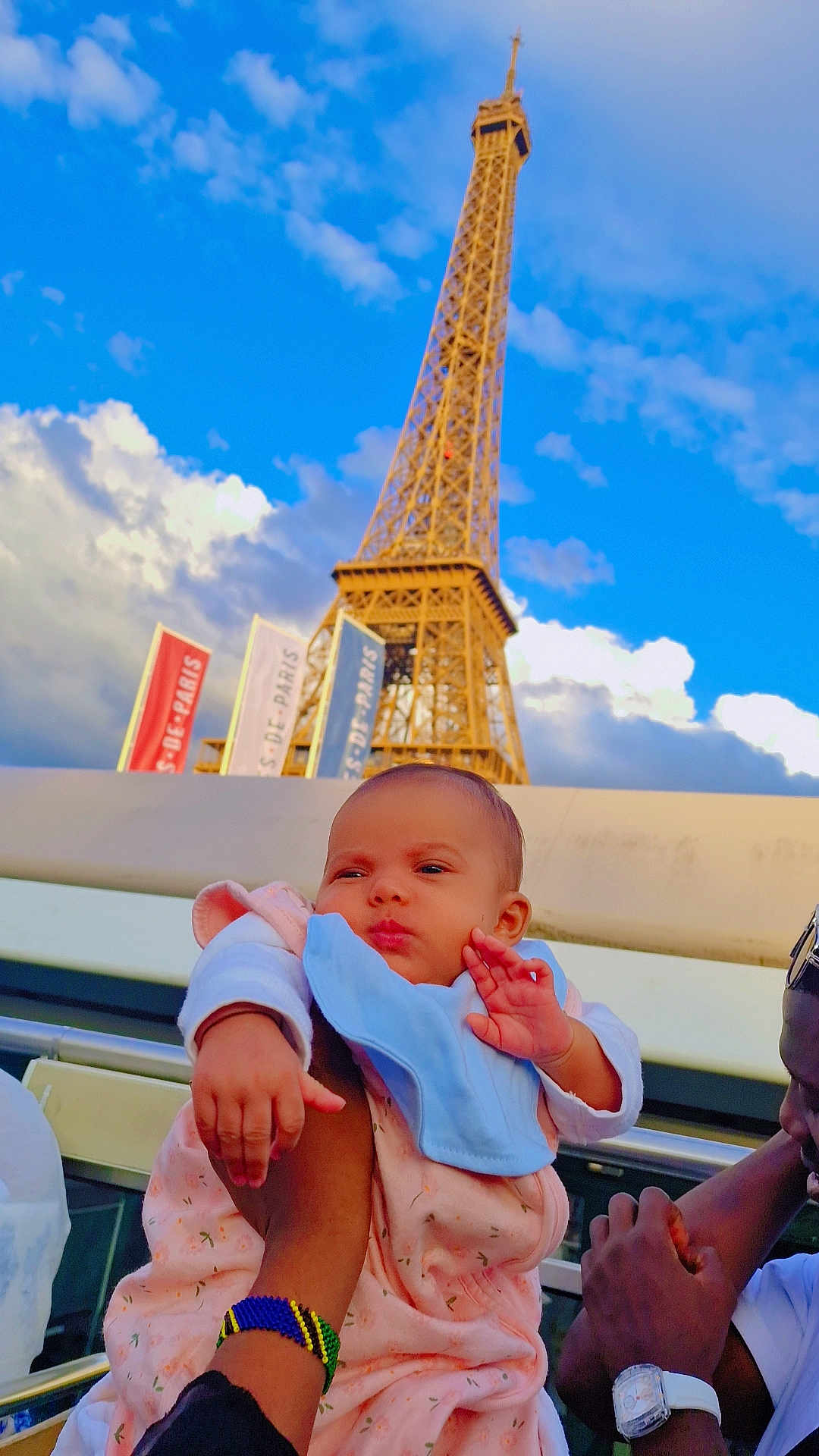 Ella a rejoint le concours — aidez-le/la à gagner de superbes lots ! baby, child, person, eiffel_tower, landmark, sky, cloud, outdoor, daylight, travel, tourist, holding, bib, blanket, arm, watch, bracelet, hand, portrait, expression