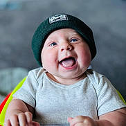 Brennan is registered to the contest to win money with this photo: baby, infant, child, smiling, laughing, blue_eyes, beanie, hat, ribbed_shirt, short_sleeve, happy, cute, hands, face, portrait, indoor, blurry_background, young, person, seated