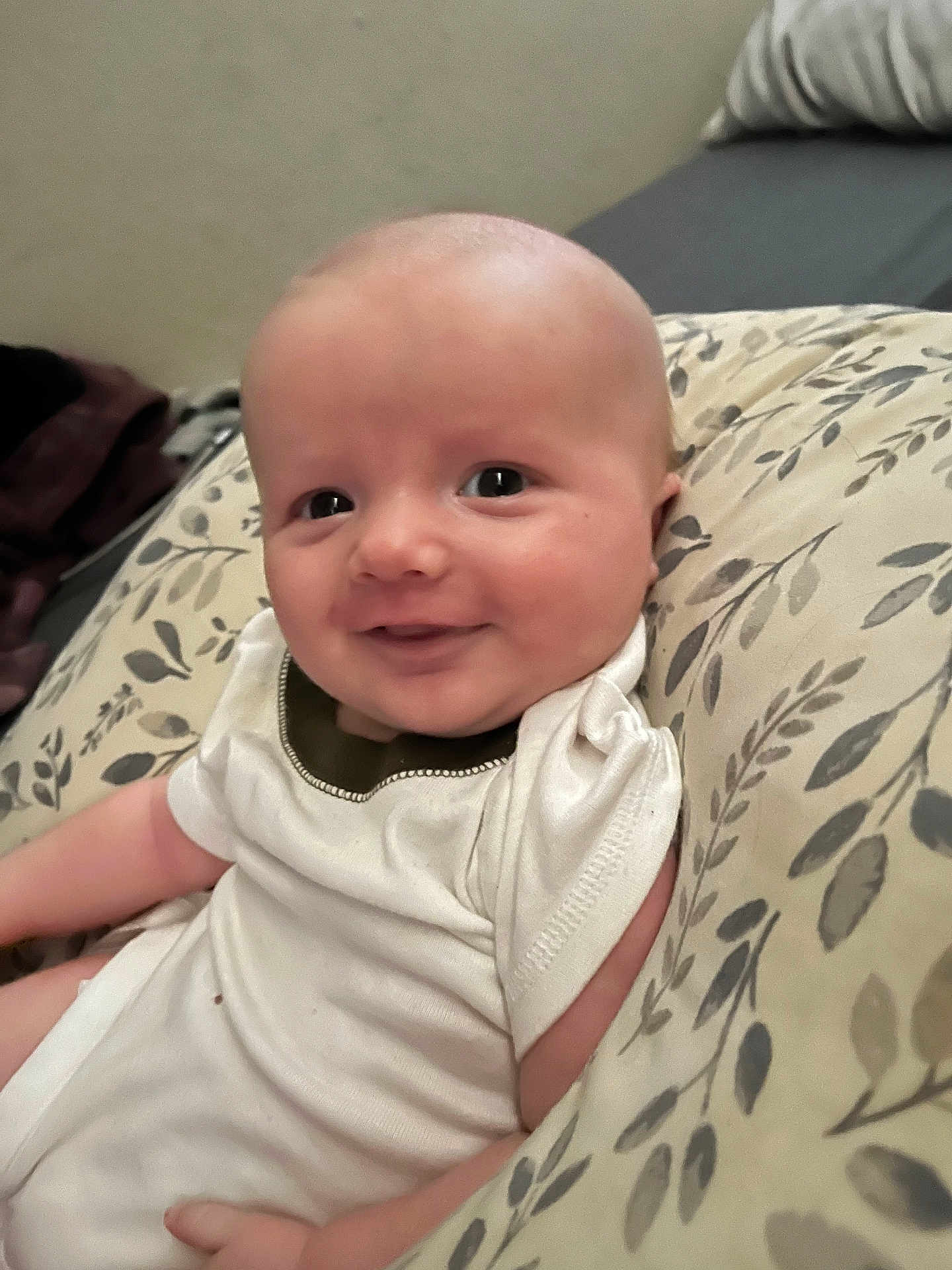 Bronson is registered to the contest to win money with this photo: baby, infant, smile, cushion, onesie, face, skin, child, comfort, happy, portrait, indoors, person, young, cute, expression, head, sitting, clothing, soft