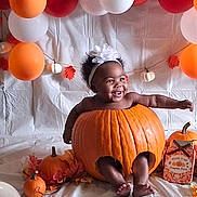 Ruth is registered to the contest to win money with this photo: baby, pumpkin, balloon, orange, white, headband, smile, autumn, fall, leaf, decoration, cute, child, celebration, festive, holiday, background, sitting, portrait, indoor