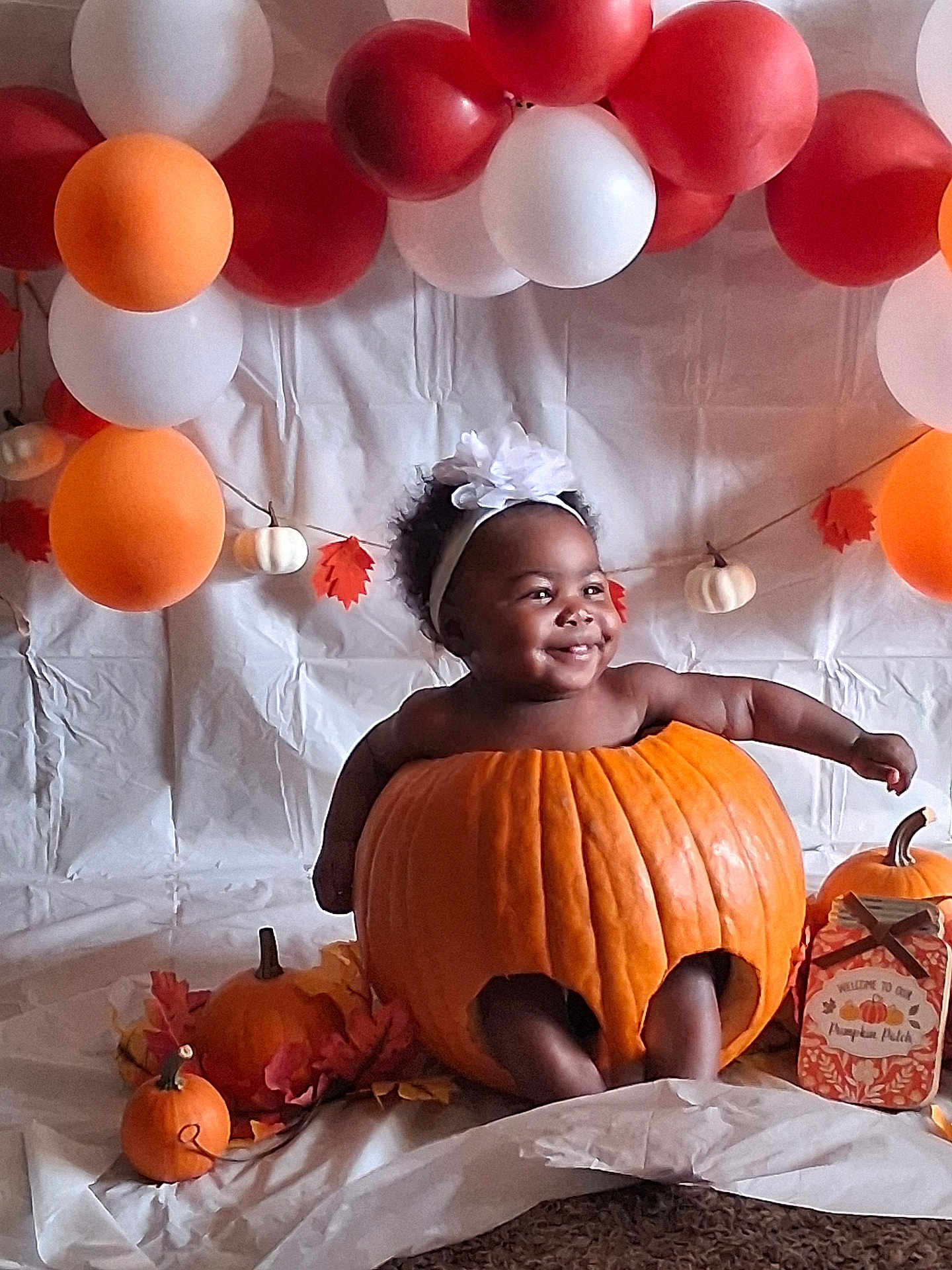 Ruth is registered to the contest to win money with this photo: baby, pumpkin, headband, smile, balloon, orange, white, fall_leaves, autumn, child, decoration, happy, holiday, cute, portrait, indoor, festive, celebration, pumpkin_patch, costume