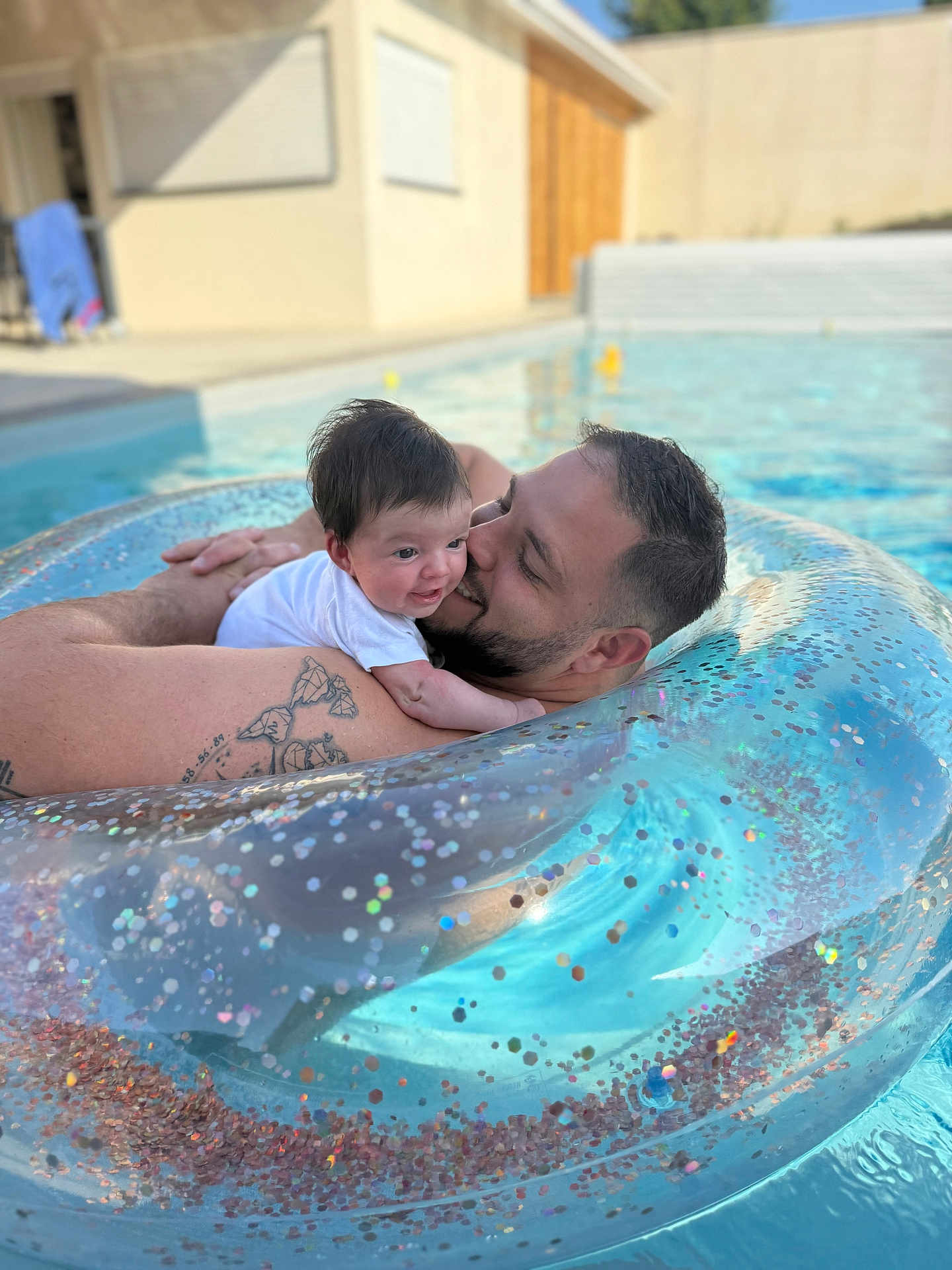 Line Lassave participe au concours pour gagner de l'argent avec cette photo : baby, man, pool, inflatable_ring, water, smile, tattoo, outdoor, sunlight, happy, family, floating, summer, relaxation, skin, person, head, face, love, leisure