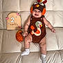 baby, infant, couch, turkey_hat, brown_outfit, white_socks, wooden_sign, 2_months, pink_butterflies, squash, milestone, smiling, cute, indoor, soft_furniture, child, holiday_theme, portrait, celebration, cozy