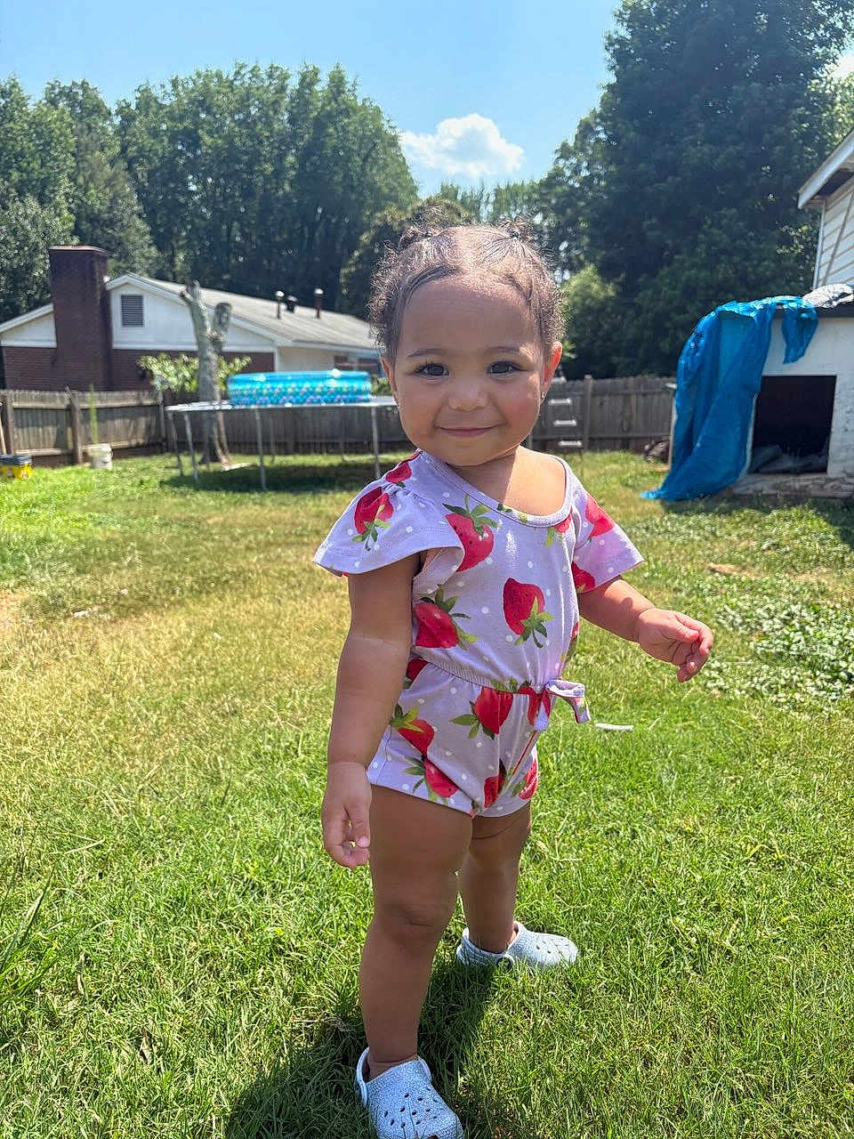 Annalise is registered to the contest to win money with this photo: toddler, child, grass, backyard, sunny, romper, strawberry_pattern, shoes, crocs, smile, happy, outdoor, daylight, person, small_child, nature, house, fence, trees, playful