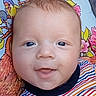 baby, infant, face, blue_eyes, smile, striped_shirt, colorful_clothing, blanket, cartoon_birds, flowers, close_up, happy, cute, child, portrait, young, skin, head, person, lying_down