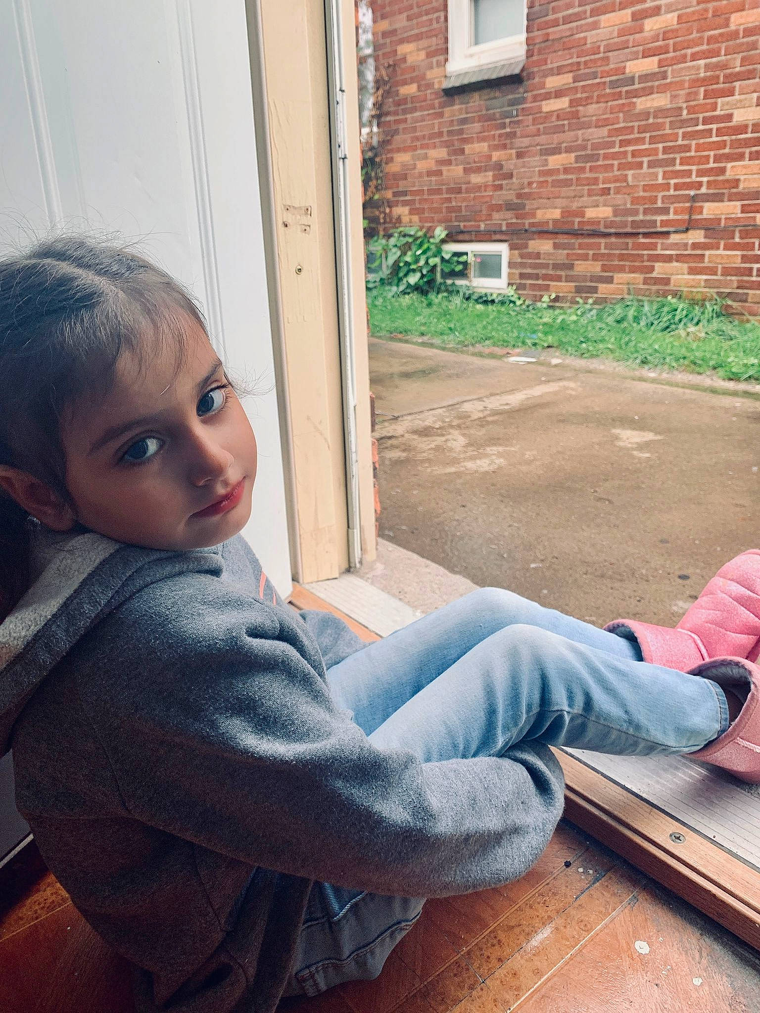 Rania is registered to the contest to win money with this photo: brickwork, child, comfort, denim, door, facial_expression, floor, flooring, fun, grass, hardwood, human_leg, joint, leisure, person, shoulder, sitting, thigh, tints_and_shades, window