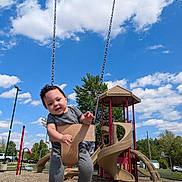 Branson joined the competition — help win amazing prizes! toddler, child, swing, playground, slide, outdoor, sky, clouds, trees, grass, play_equipment, daytime, happy, smiling, casual_clothing, footwear, park, fun, activity, person