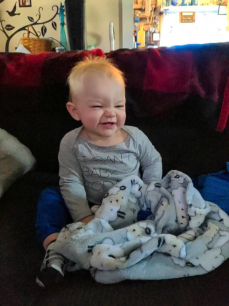 Koemason is registered to the contest to win money with this photo: baby, baby_toddler_clothing, bookcase, child, comfort, couch, fun, happy, head, holiday, lamp, linens, living_room, person, picture_frame, room, sitting, skin, smile, t_shirt