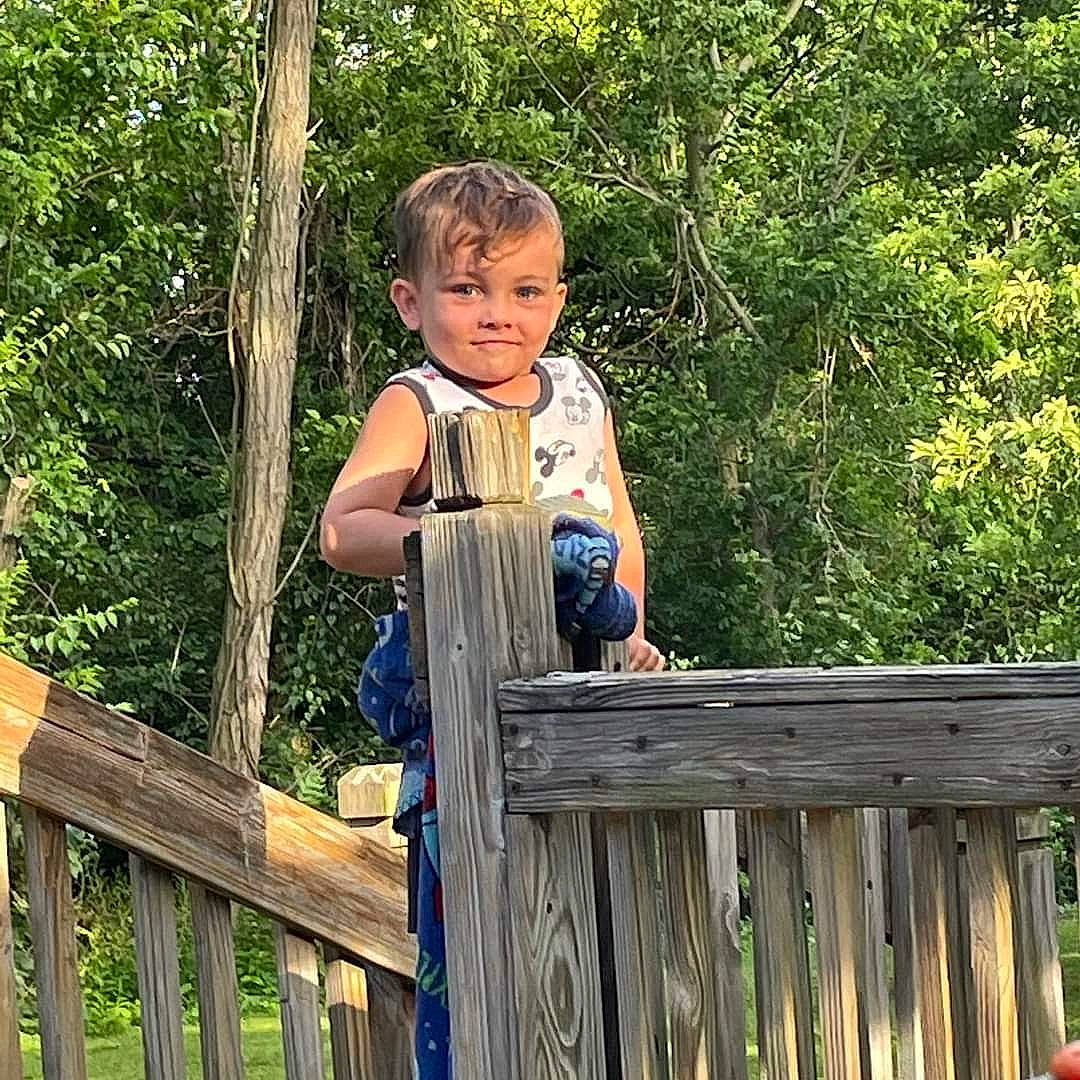 Khyri is registered to the contest to win money with this photo: baby_toddler_clothing, child, fence, forest, fun, grass, happy, joy, leisure, people_in_nature, person, shorts, sitting, sleeve, t_shirt, toddler, tree, vacation, wood