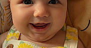 Oakley is registered to the contest to win money with this photo: baby, infant, child, smiling, happy, portrait, closeup, face, eyes, bow, headband, sunflower, dress, overalls, floral_pattern, button, sitting, bedding, stuffed_toy, indoor