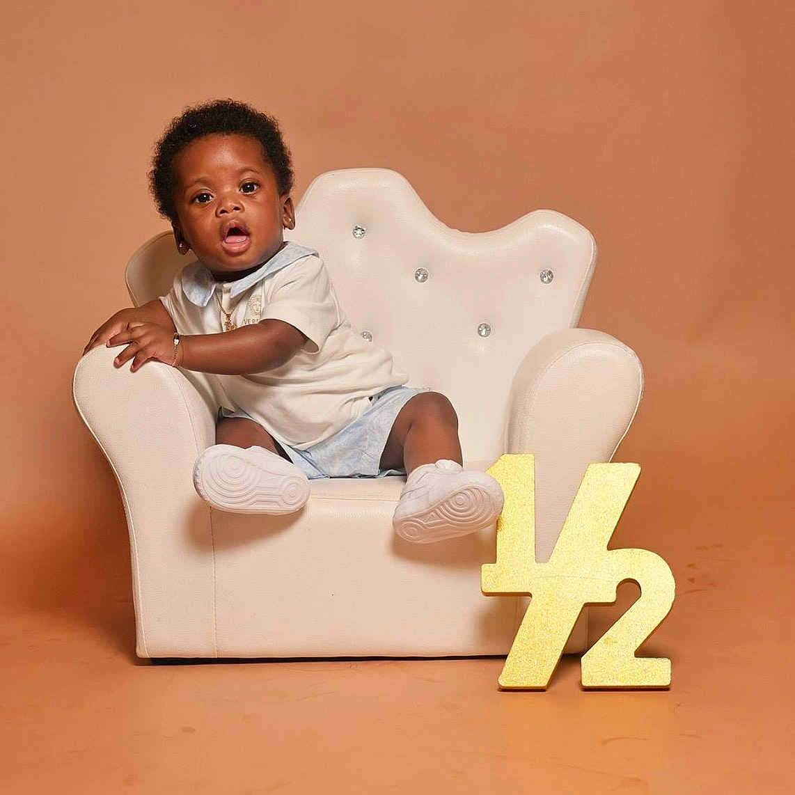 Rushawn joined the competition — help win amazing prizes! toddler, child, armchair, white_chair, plush, half_year, gold_sign, curly_hair, shorts, sneakers, bracelet, neutral_background, studio_photo, portrait, cute, celebration, baby, sitting, expression, indoor