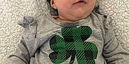 Arya is registered to the contest to win money with this photo: baby, infant, child, blanket, headband, bow, shamrock, plaid, green, gray_shirt, onesie, lying_down, close_up, chubby_cheeks, big_eyes, hand, fingers, cozy, portrait, soft_texture