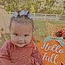 autumn, baby, backyard, bow, child, dress, face, fall, hair_bow, infant, outdoor, pink_outfit, portrait, pumpkin, seasonal_decor, sitting, smiling, sunlight, trees, white_fence