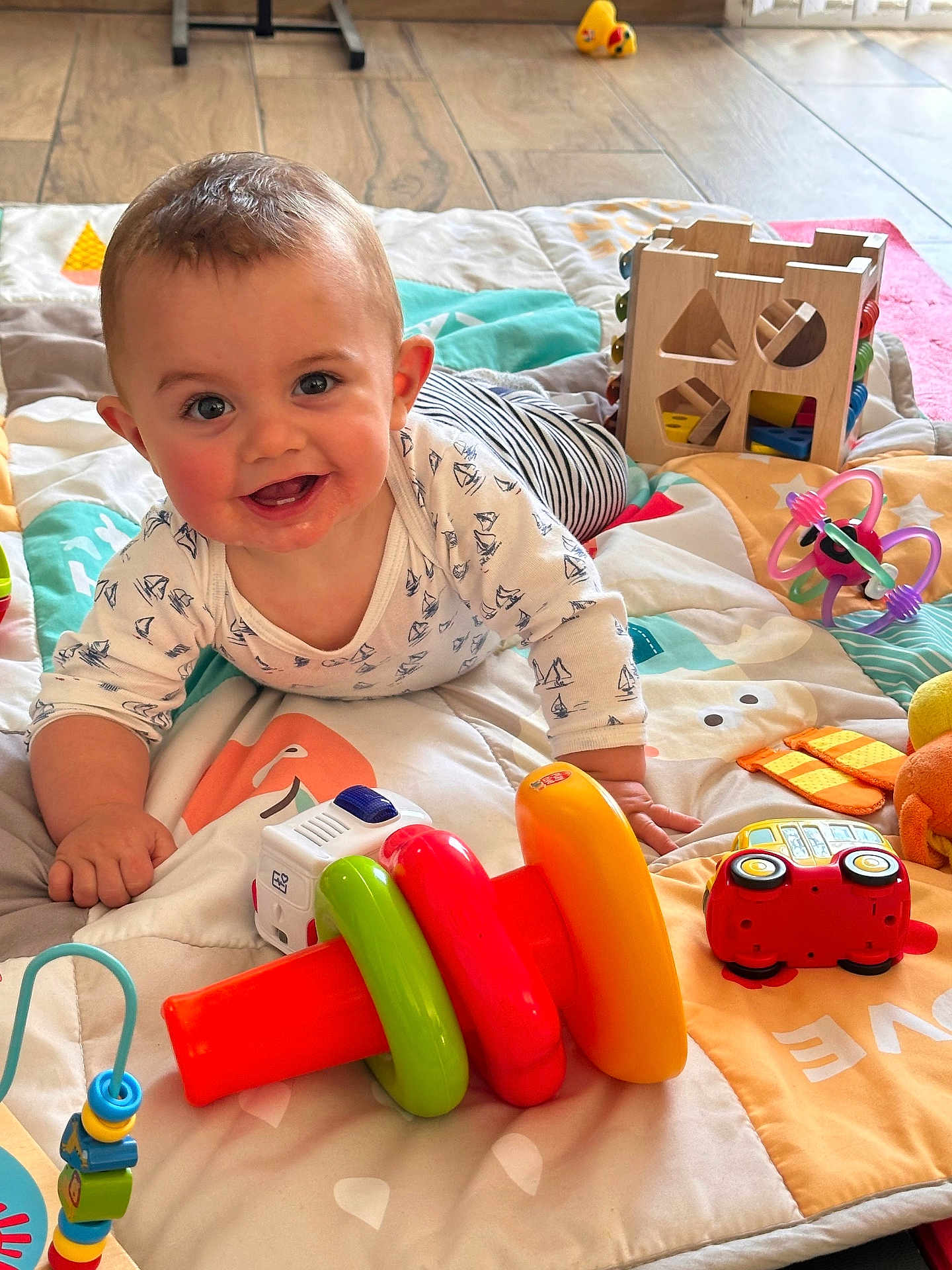 Malo a rejoint le concours — aidez-le/la à gagner de superbes lots ! baby, smiling, play_mat, toy, stacking_rings, wooden_toy, indoor, child, crawling, colorful, floor, happy, person, cute, toddler, clothing, face, hand, playtime, bright