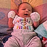baby, child, clothing, colorful_text, cozy, cute, face, happy, indoors, infant, lying_down, mittens, newborn, onesie, patterned_blanket, person, portrait, small_but_fierce, smiling, soft_toys