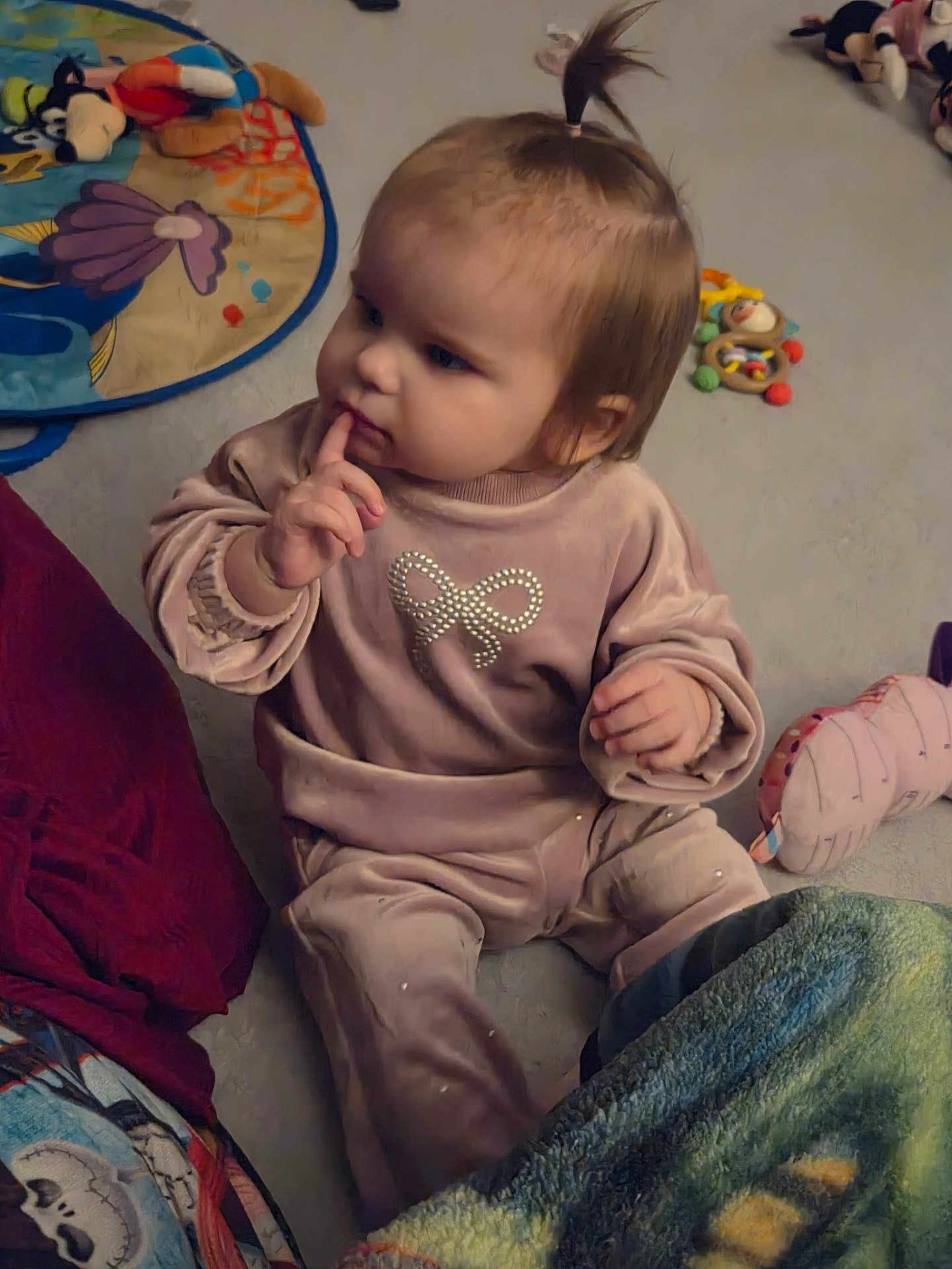 Autumn is registered to the contest to win money with this photo: child, baby, toddler, sitting, indoor, toy, plush, playmat, blanket, onesie, bow_design, finger_on_mouth, thoughtful, hair_ponytail, carpet, portrait, cute, soft_lighting, rattle, floor