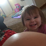 Autumn is registered to the contest to win money with this photo: toddler, child, smile, face, indoor, carpet, toy, living_room, furniture, blanket, curtain, person, hair, clothing, happy, mouth, nose, eye, finger, home