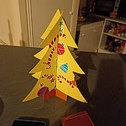 Louna a rejoint le concours — aidez-le/la à gagner de superbes lots ! building, christmas, christmas_decoration, christmas_ornament, christmas_tree, cone, creative_arts, event, evergreen, flooring, holiday, ornament, plant, shelf, tints_and_shades, tree, triangle, window, wood, woody_plant