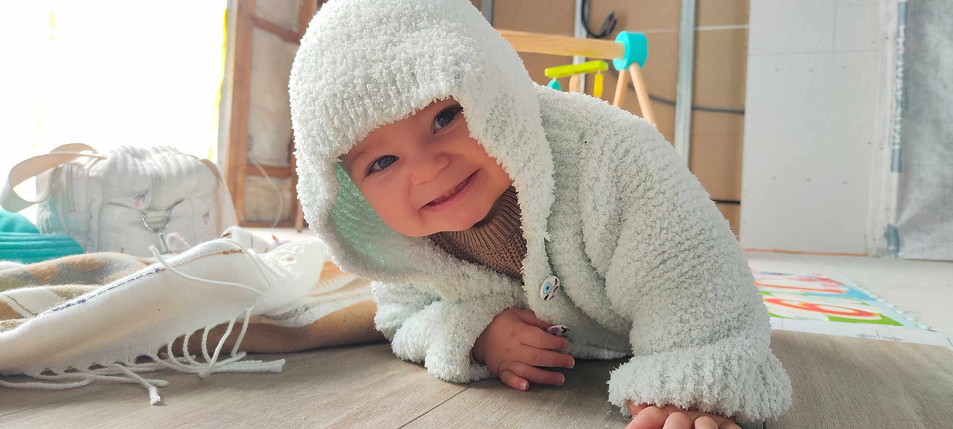 Jade participe au concours pour gagner de l'argent avec cette photo : baby, child, hoodie, crawling, floor, smile, indoor, blanket, toy, playgym, wooden_floor, cute, warm_clothing, happy, infant, cozy, button, person, portrait, toddler