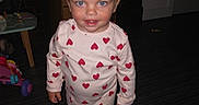 Skyla is registered to the contest to win money with this photo: toddler, child, pajamas, hearts, barefoot, indoor, floor, toy, blanket, pigtails, pink, blue_eyes, smiling, person, clothing, striped_floor, playroom, furniture, curious, standing