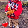 child, red_jacket, spiderman, plush_toy, winter_hat, outdoor, muddy_ground, sneakers, beige_pants, tree, grass, leafless_trees, smiling, cute, playful, winter_clothing, person, nature, heart_emoji, daytime
