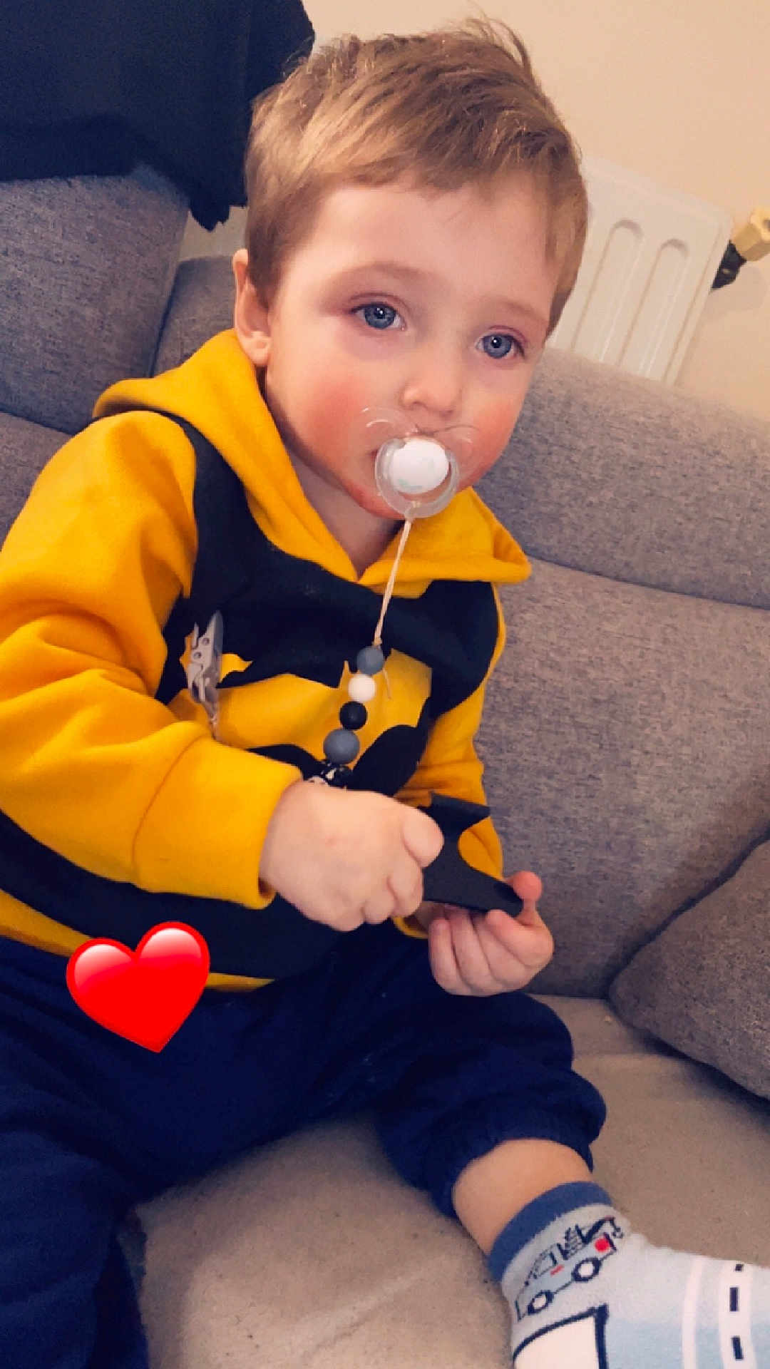 Loevan participe au concours pour gagner de l'argent avec cette photo : toddler, child, pacifier, hoodie, yellow_clothing, blue_eyes, indoor, couch, sitting, cute, sock, toy, face, hand, person, cozy, radiator, red_heart_emoji, casual_clothing, young_child