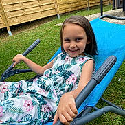 Lynezia participe au concours pour gagner de l'argent avec cette photo : child, girl, smiling, outdoor, grass, fence, chair, blue_chair, floral_dress, happy, casual, summer, relaxing, person, hand, nature, leisure, portrait, daylight, fun