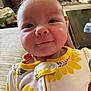 baby, child, clothing, cute, face, flower_pattern, furniture, hair, hand, happy, head, indoor, infant, onesie, person, pet, portrait, skin, smile, yellow